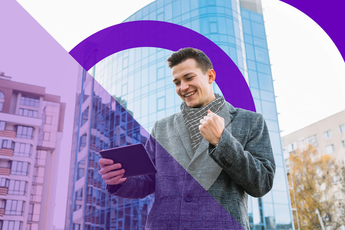 An excited young man looking at his tablet outside.