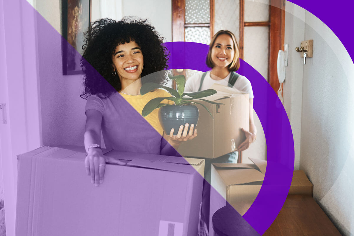 Two women carrying moving boxes into a home.